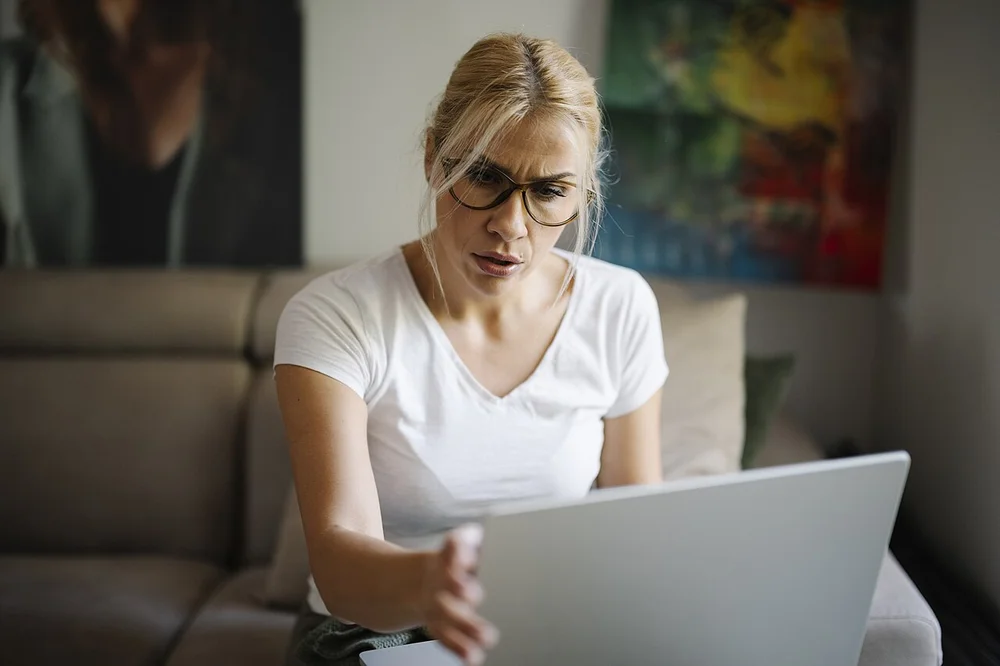 angry facial expression photo — Angry woman using laptop at home while sitting on couch