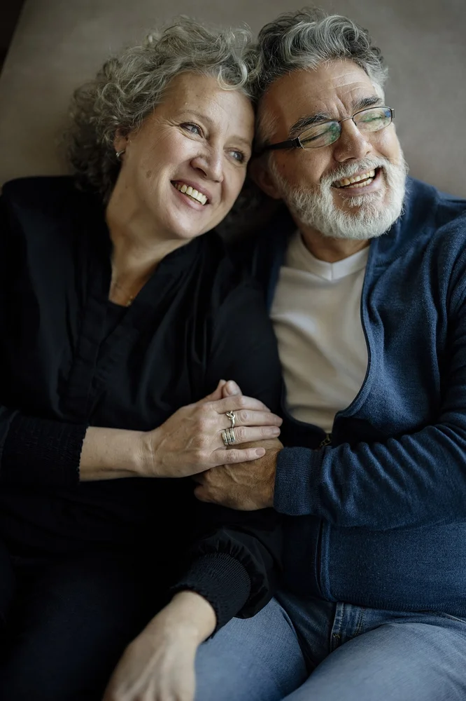 happy facial expression photo — Couple sits close together on a couch smiling and holding hands