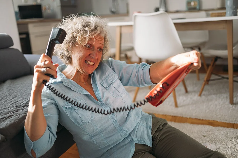 angry facial expression photo — Frustrated woman struggles with a tangled phone cord while sitting comfortably a